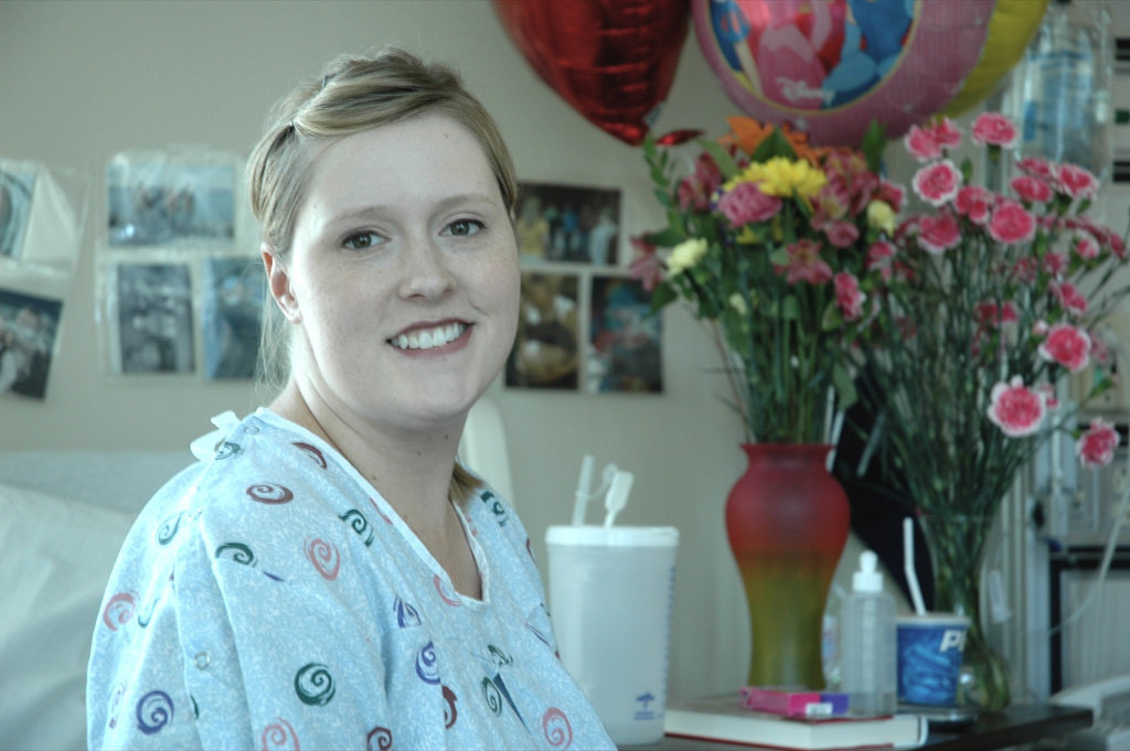 New mum in hospital room surrounded by flowers and balloons. Adelaide postnatal doula Kelly Harper Elemental Beginnings