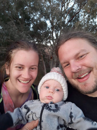First time parents smiling at the camera with their baby girl in between them. Happy clients of Adelaide doula, Kelly from Elemental Beginnings