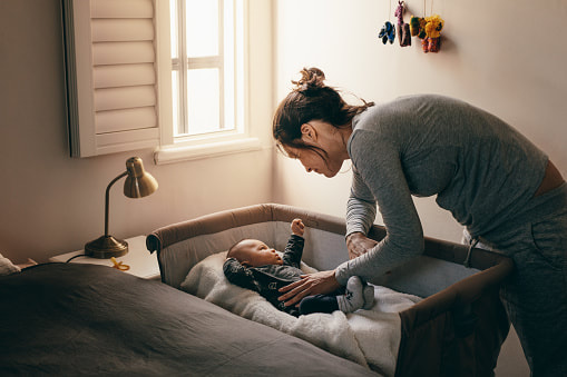 Mother putting baby down to sleep in cosleeper next to her bed | Sleep help Adelaide